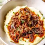 Delicious beef stew served over creamy mashed potatoes, topped with fresh parsley. Perfect comfort food meal.
